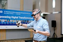 An illustrative photo of  a man in a plaid shirt holds a black and brown corded microphone and wear VR glasses