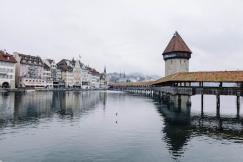 An illustrative photo of body of water near concrete buildings under white and gray sky at daytime.