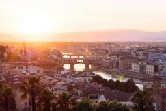 An illustrative photo of the city’s historic architecture and the Arno River under a warm sunset in Florence, Italy