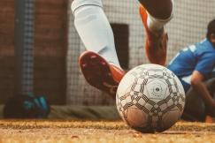 An illustrative photo of a person in a white and red soccer jersey is captured mid-kick with a soccer ball 