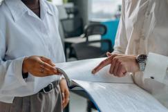 An illustrative photo of two colleagues in white long-sleeve shirts standing together, discussing and reading a financial report