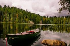 An illustrative photo of a canoe on lake near trees.