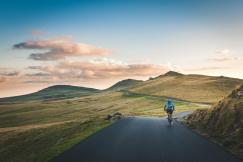 An illustrative photo of a person cycling on a road with a distant mountain range in the background