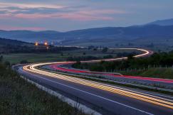 An illustrative photo of a highway at dusk or early evening, capturing the light trails of vehicles