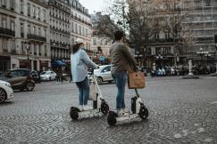 An illustrative photo of two individuals riding electric scooters on a paved street