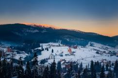 An illustrative photo of snowy mountain surrounded of larch trees.