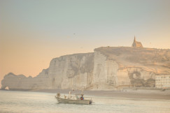 An illustrative photo of a boat in the body of water with cliffs in the background during sunset