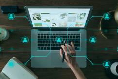 An illustrative photo of a person using a laptop on a wooden desk, surrounded by various objects and digital graphics
