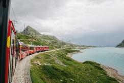 An illustrative photo of a red train on rail near body of water.