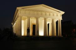 An illustrative photo of a neoclassical building illuminated at night with a silhouette of a person standing in the entrance