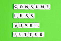 An illustrative photo of white tiles with black letters spelling out the phrases “CONSUME LESS,” “SHARE MORE,” and “LIVE BETTER” against a bright green background