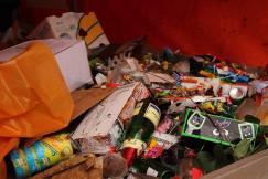 An illustrative photo of a large pile of unsorted trash, including cardboard boxes, plastic containers, and glass bottles