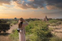 An illustrative photo of a woman wearing a straw hat and a dress, taking a photograph of a landscape