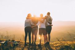 An illustrative photo of four person hands wrap around shoulders.
