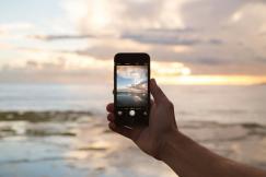 An illustrative photo of a person holding smartphone showing ocean.