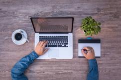 An illustrative photo of a person typing on a laptop while writing notes