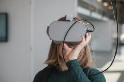 An illustrative photo of a woman in a black sweater holding white and black VR goggles