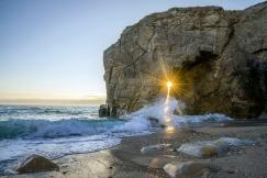 An illustrative photo of sea wave splashing in seashore beside mountain.