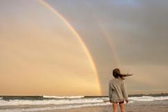 An illustrative photo of a woman standing on shore with rainbow