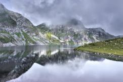 An illustrative photo of a tranquil mountain lake with a reflection of the surrounding peaks and clouds