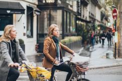 An illustrative photo of two women riding their bikes along a city street