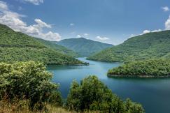 An illustrative photo of a lake nestled within a valley, surrounded by lush green hills under a partly cloudy sky