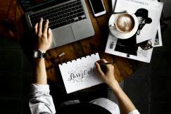 An illustrative photo of a person working on a laptop with coffee and a magazine on a wooden table