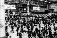 An illustrative photo of people walking through a train station in grayscale