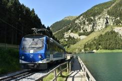 An illustrative photo of train on rail tracks near body of water.