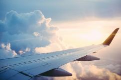 An illustrative photo of an airplane wing in the sky with clouds
