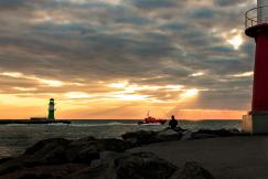 An illustrative photo of a red lighthouse standing on top of a rocky shore near body of water during sunset
