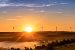 An illustrative photo of sunset over a landscape with wind turbines and misty valleys