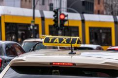 An illustrative photo of the top of taxi with a sigh with vehicles and a tram in the background
