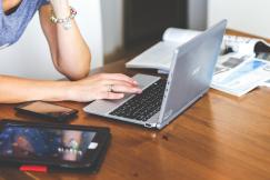 An illustrative photo of a person working on the laptop with a phone and a tablet on the table