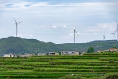 An illustrative photo of a rural landscape with terraced fields and wind turbines in the background
