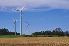 An illustrative photo of wind turbines standing tall in a plowed field under a clear blue sky