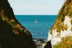 An illustrative photo of a boat in the water near a cliff.