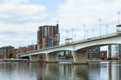 An illustrative photo of a bridge over a body of water with tall buildings in the background
