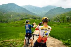 An illustrative photo of a couple of people on bikes on a dirt road with mountains in the background