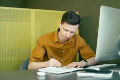 An illustrative photo of a man taking notes in front of his computer