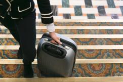 An illustrative photo of a person rolling a suitcase into hotel