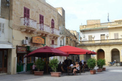 An illustrative photo of people sitting in an outside cafe under red umbrellas