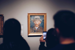 An illustrative photo of a person taking picture of a painting of a man wearing brown hat in museum