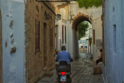 An illustrative photo of a man riding a motorcycle down a narrow alley way