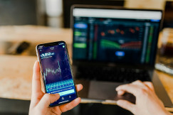 An illustrative photo of a person looking at graphs on a phone and on a laptop