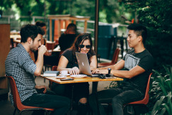 An illustrative photo of three people sitting in a cafe while working and talking 