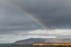 An illustrative photo of a rainbow in the sky over a body of water.