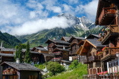 An illustrative photo of brown wooden houses near green trees and mountains