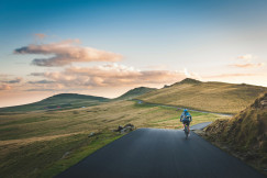 An illustrative photo of a person cycling on a road in the countryside in the mountains.