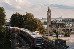 An illustrative photo of a train on rail road near brown concrete building.